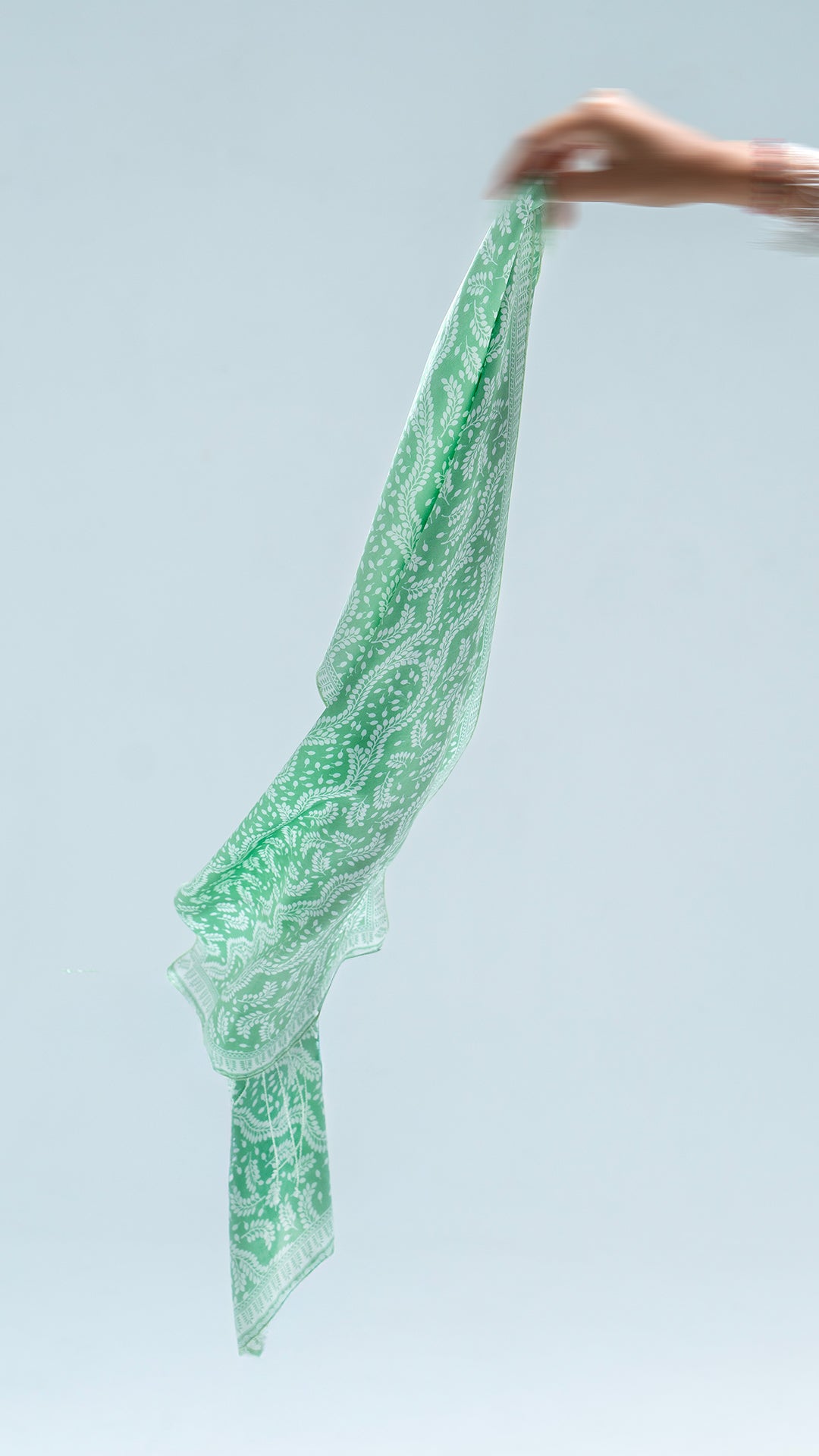 Green daun asem scarf fabric held by a hand against a light blue background