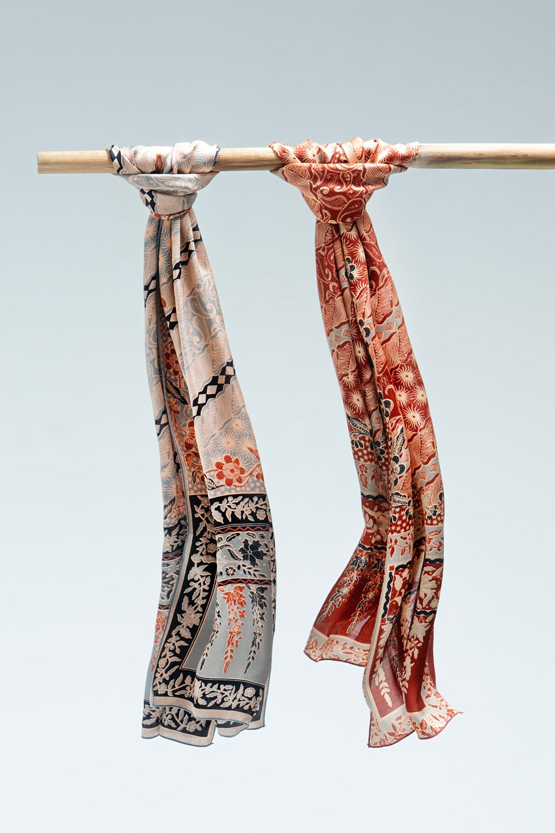 Two lengko batik scarves hanging on a rod against a light gray background