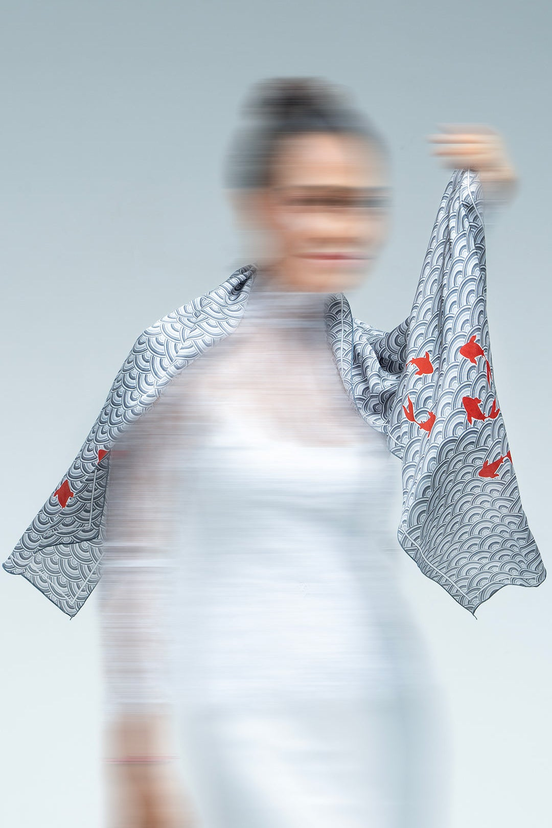 Person wearing a scarf garment with fish and Japanese patterns on a plain background
