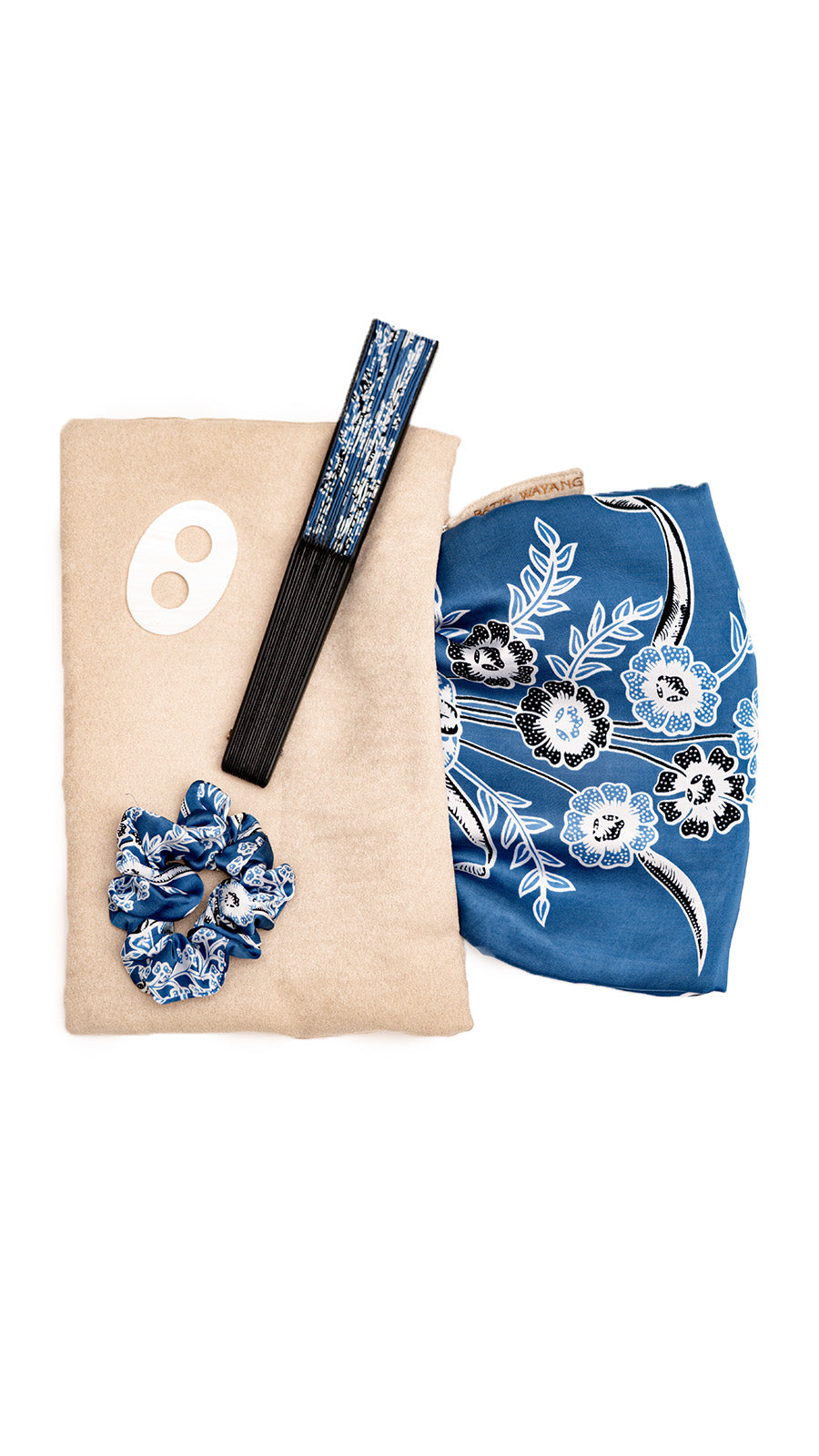 Set of sarong beach set accessories including a scrunchie, buckle and matching fan on a beige bag. 