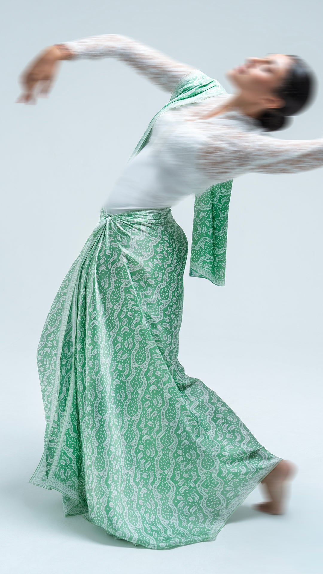 Person wearing a daun asem green scarf and sarong on a light gray background