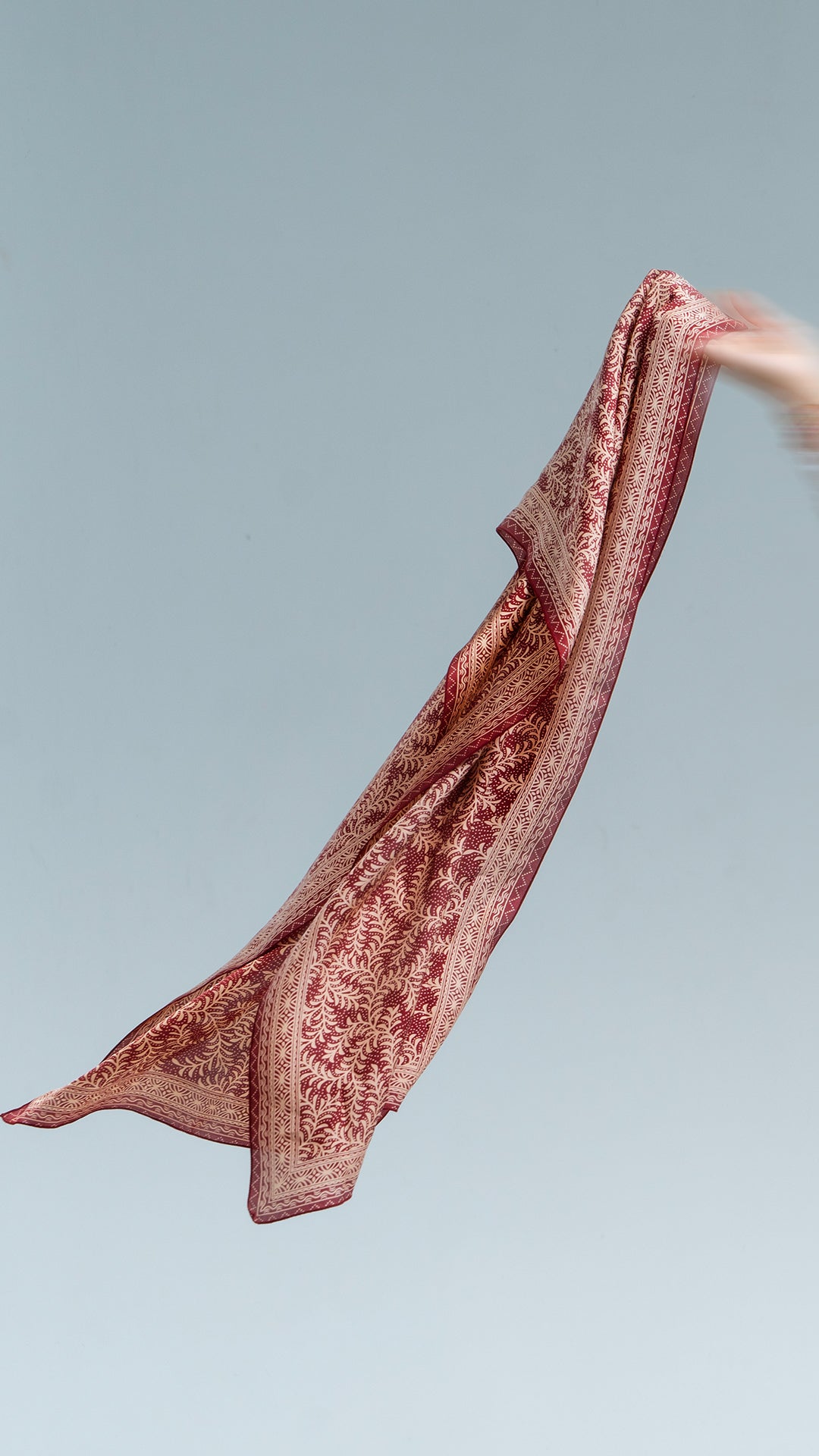 Red daun asem batik fabric held up against a gray background