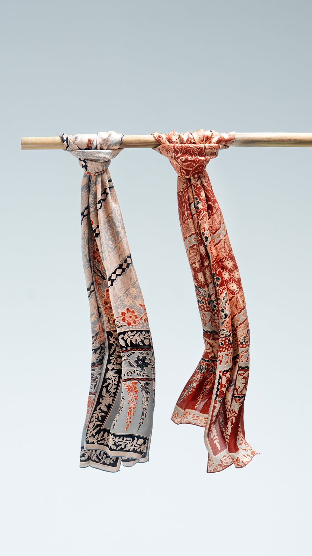 Two lengko batik scarves hanging on a rod against a light gray background