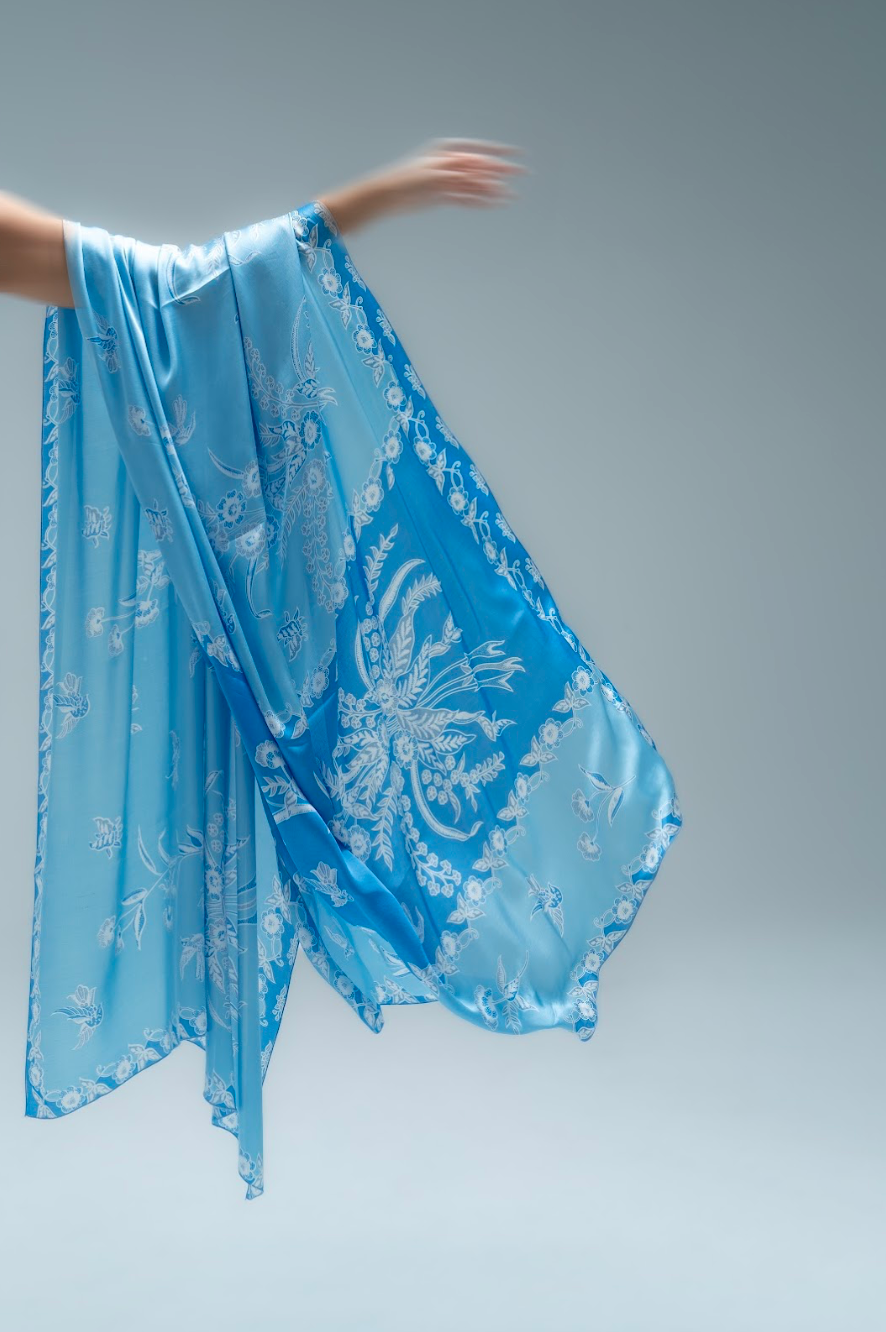 Blue sarong with white floral patterns held by a person against a gray background