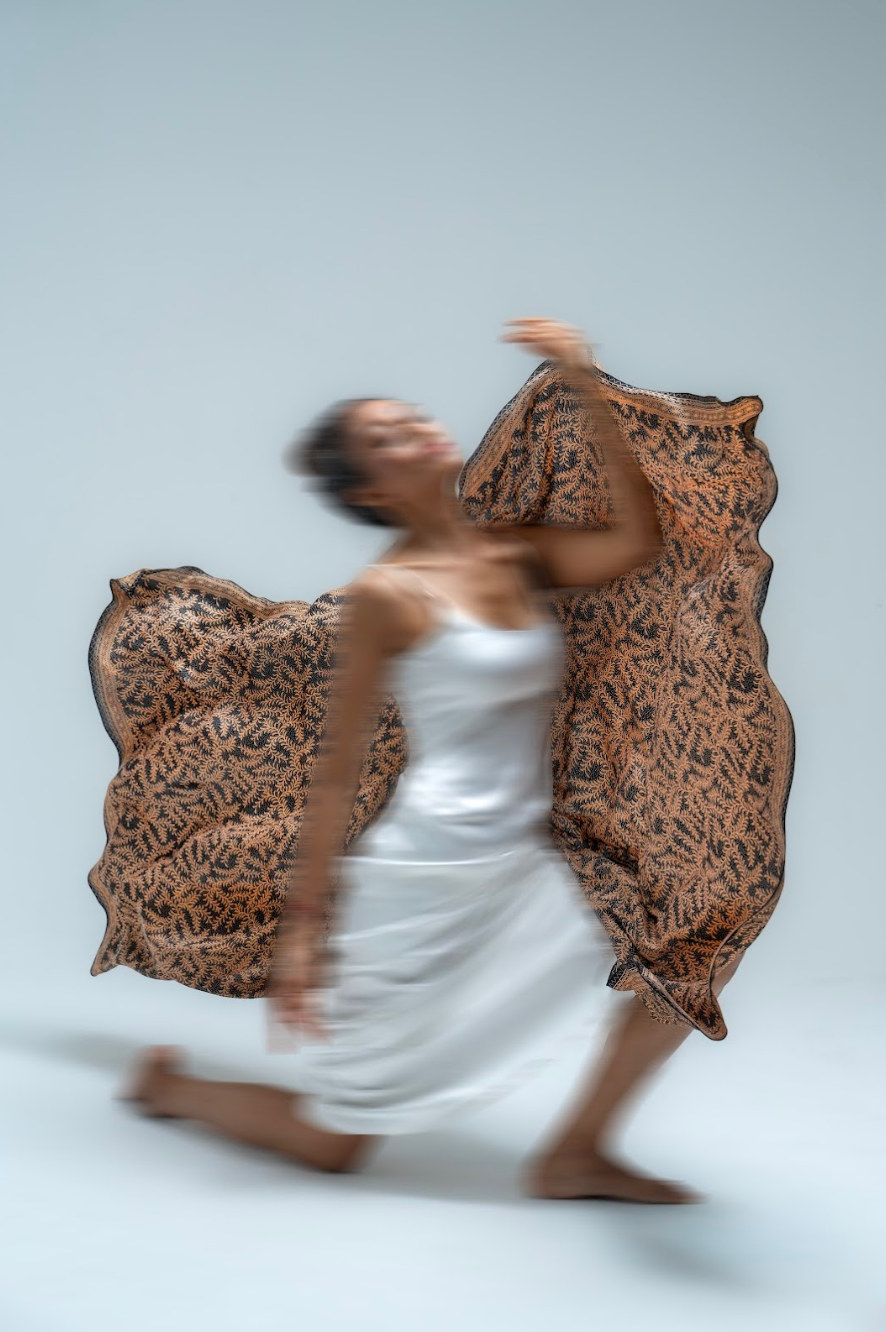 Person in a white dress with a daun asem batik print sarong over shoulders against a light gray background