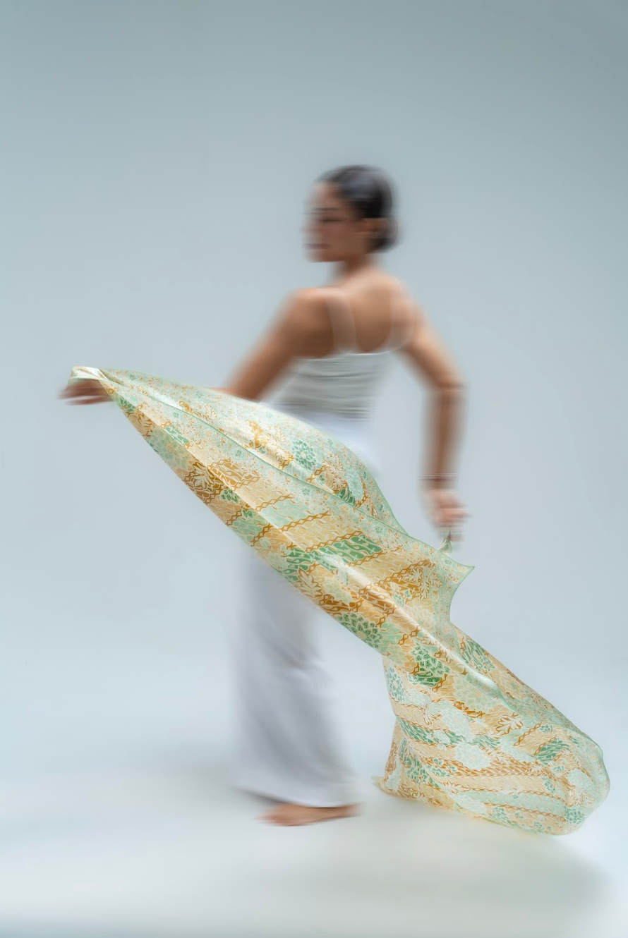 Woman holding a long, batik patterned sarong against a plain background