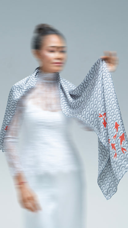 Woman wearing a patterned scarf with orange fish design on a plain background