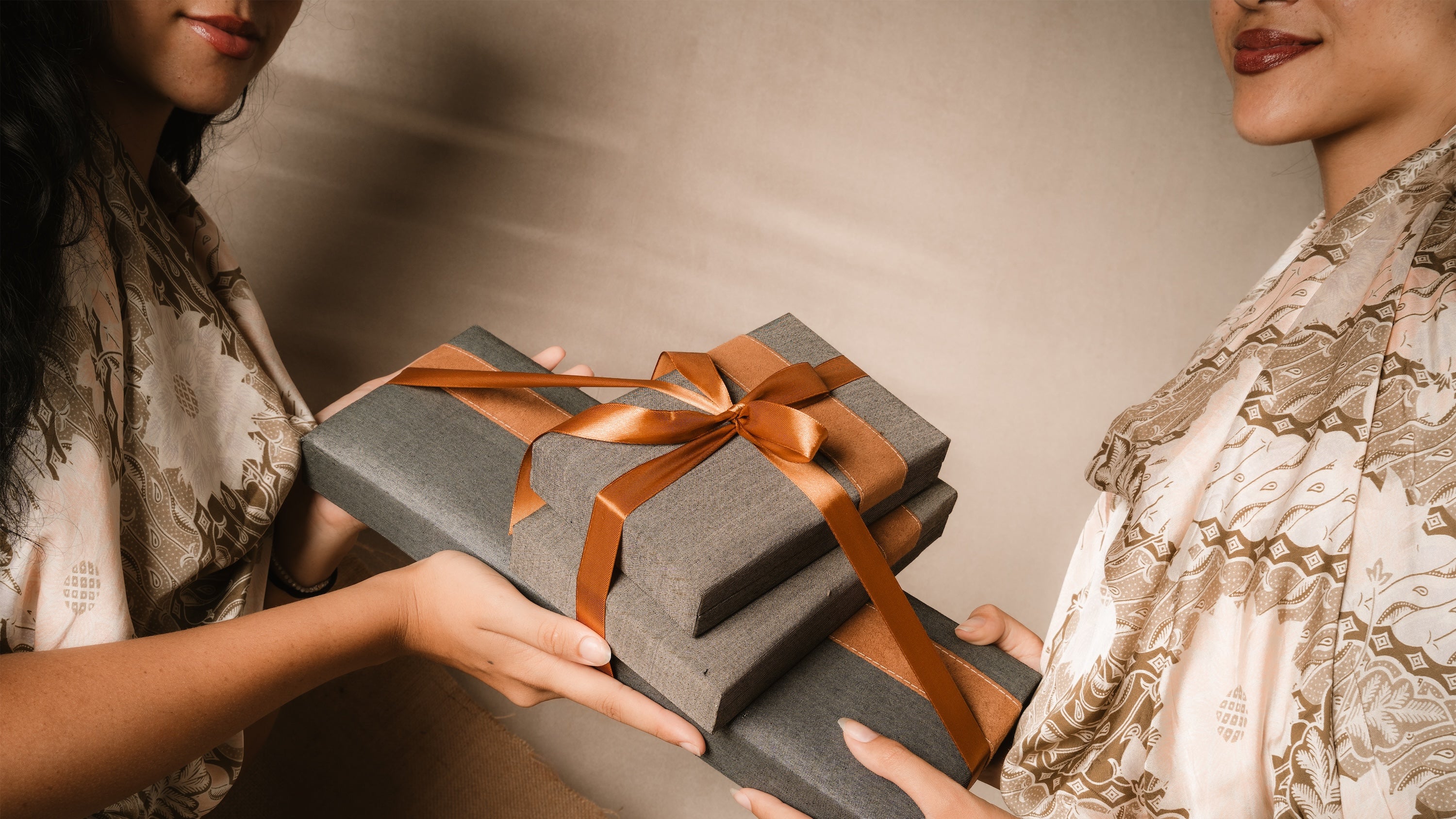Two women smiling while holding a gift box with a brown ribbon.